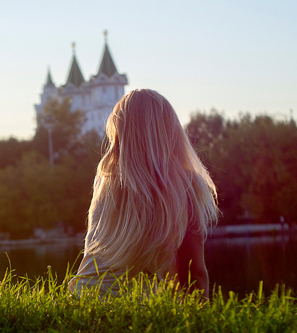 Woman with long hair sitting peacefully by a lake at sunset, reflecting